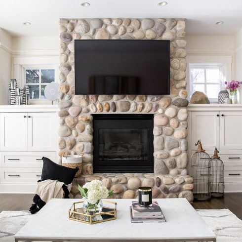 full on view of round stone fireplace with tv above and flanking white cabinets
