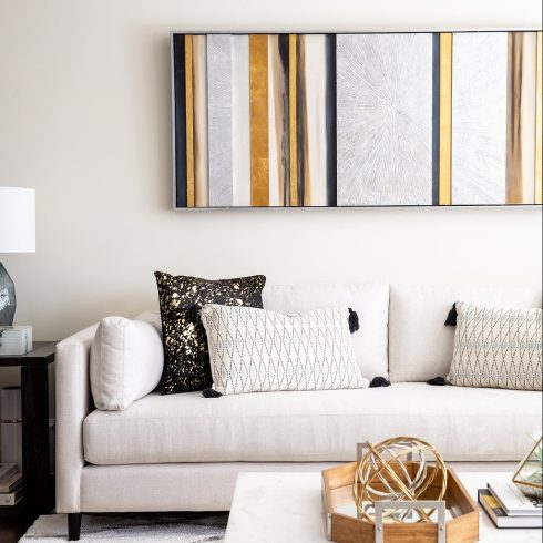 black, gold and white vertical artwork above cream sofa with cushions
