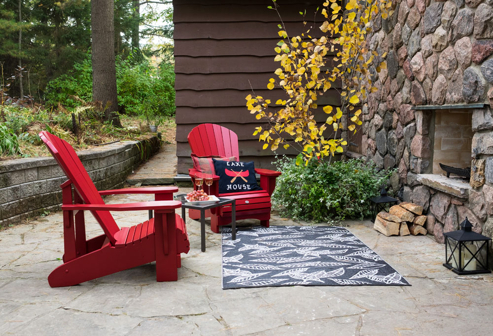 Canadian backyard with red muskoka chairs, rug and a massive stone fireplace.