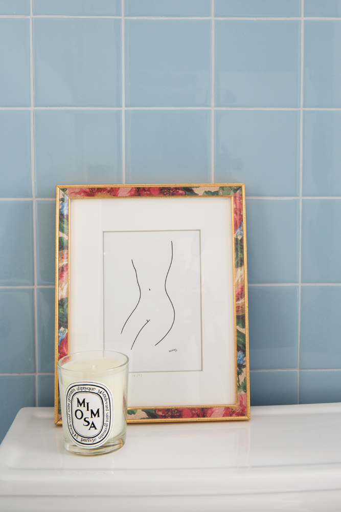 closeup of drawing and mimosa candle on toilet in blue tile bathroom