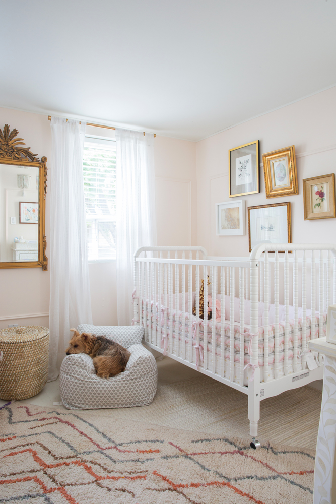 nursery with white crib, gold framed art and dog in little chair