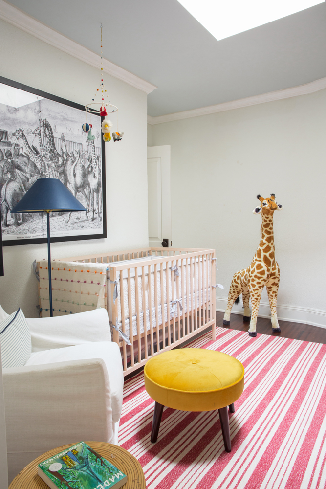 kids room with crib and stuffed giraffe in corner, yellow stool, red striped rug