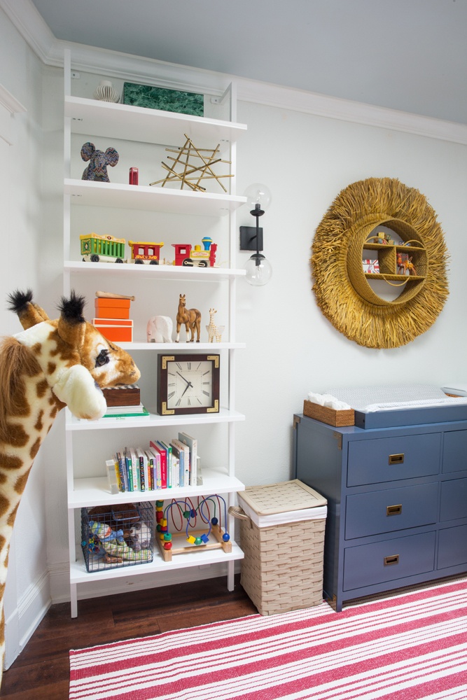 kids room with giraffe in corner, one white toy and book shelf blue dresser changing table