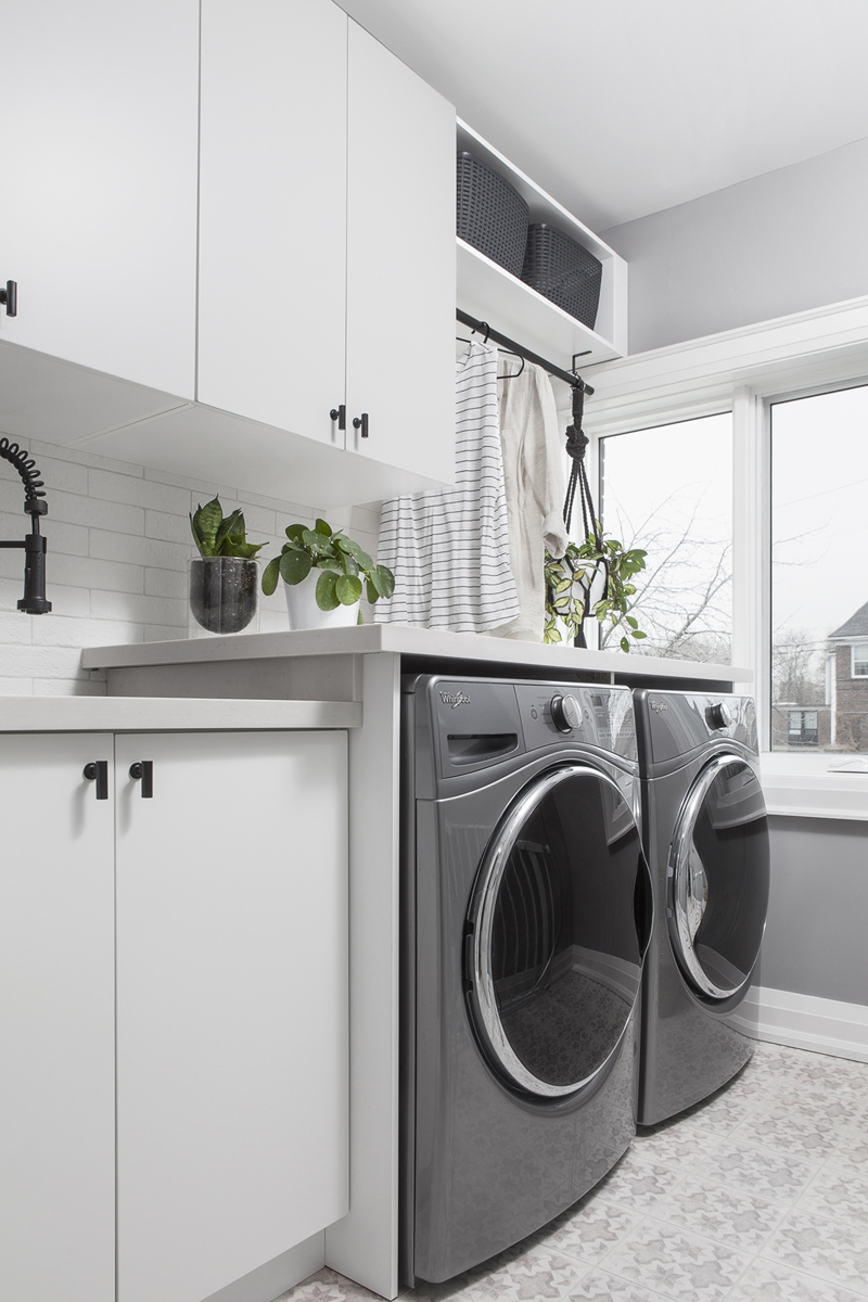 A sleek laundry room with plants, patterned tiled flooring and white cabinets
