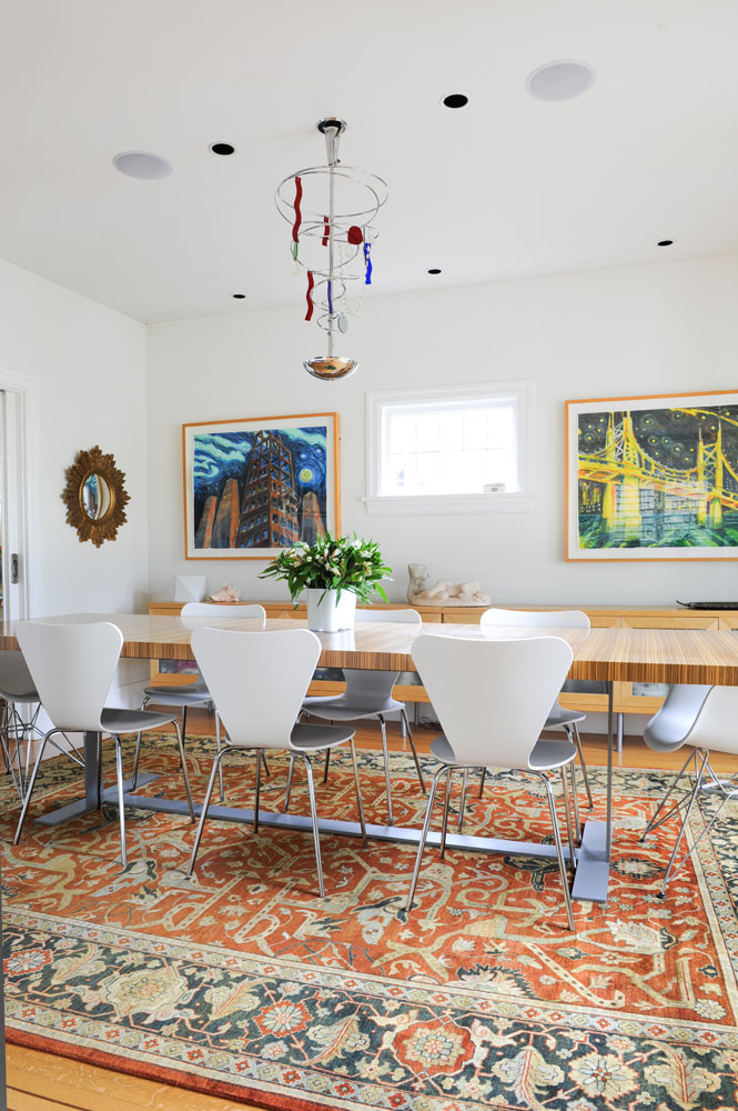 Dining room with white chairs, wood table, two paintings flanking small window