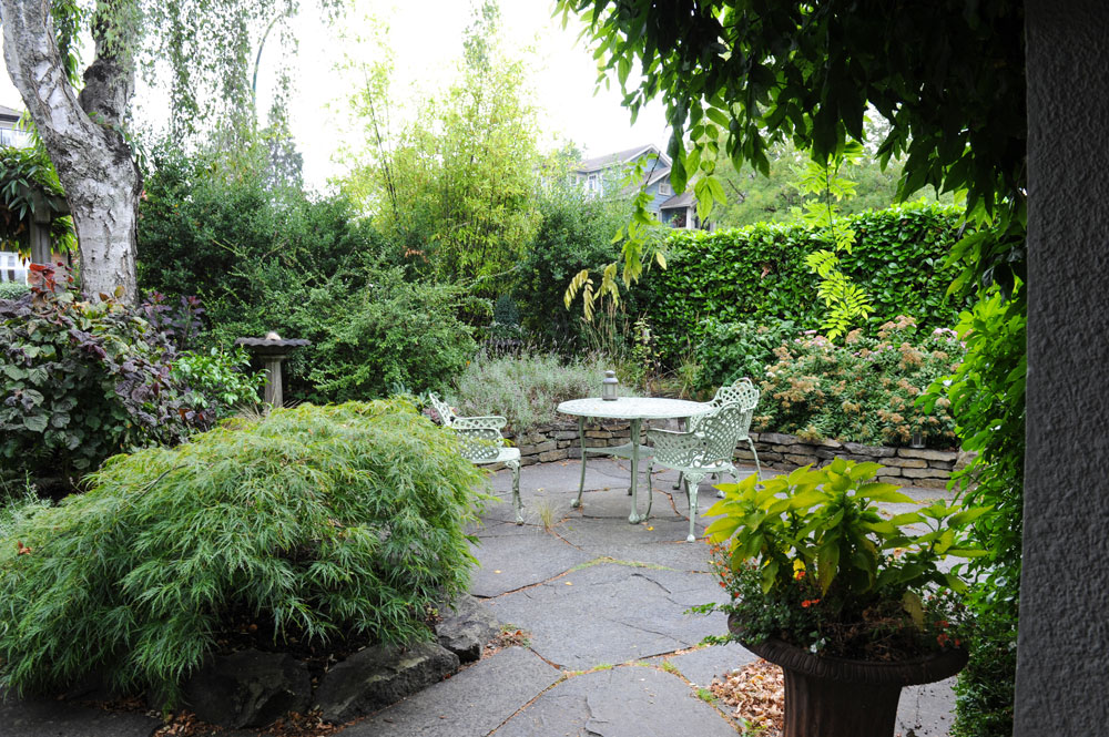 Leafy backyard with flagstones and light-green wrought iron table and chairs