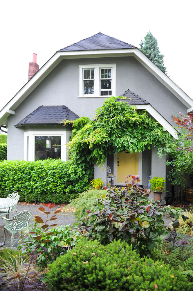 Front of grey house with yellow front door and greenery