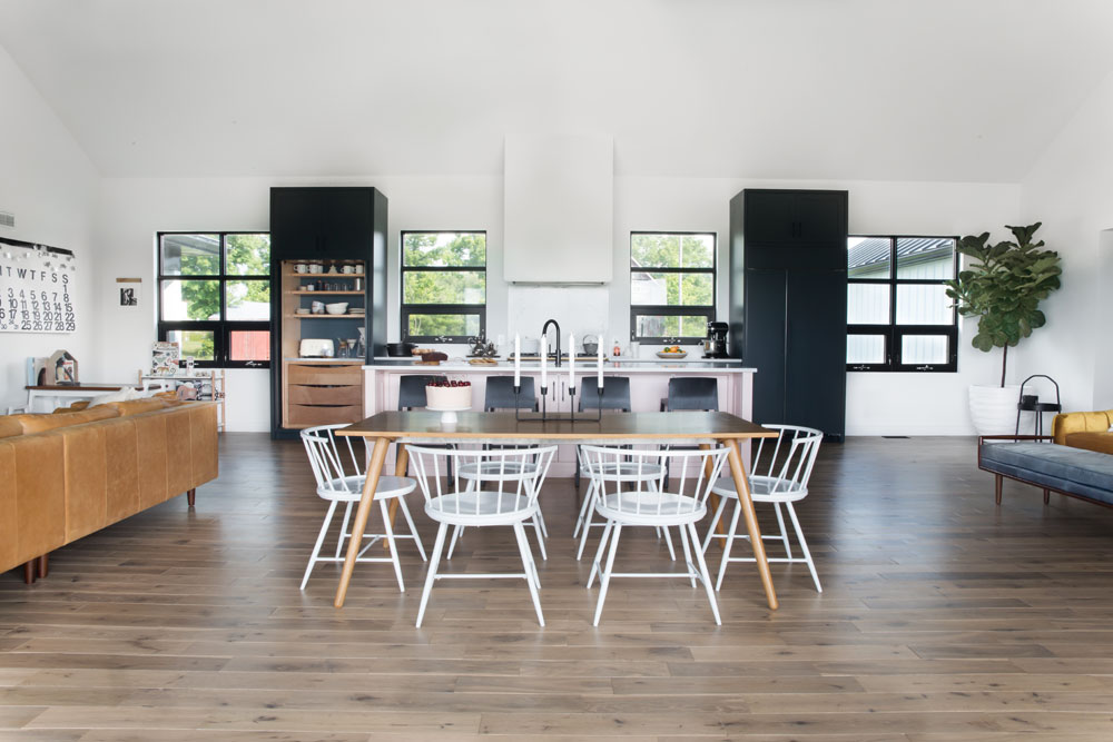open floor plan with dining table and white chairs in centre, two large black cabinets in kitchen behind
