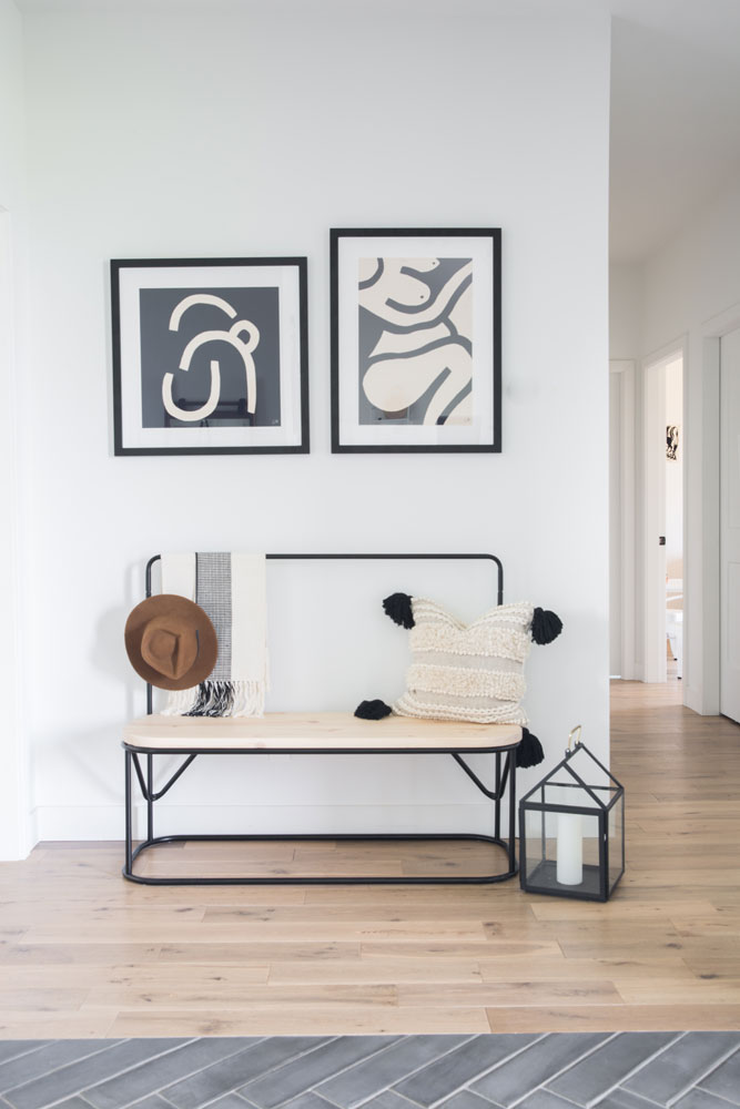 pale wood and black iron bench in entryway beneath tow black and white framed abstracts