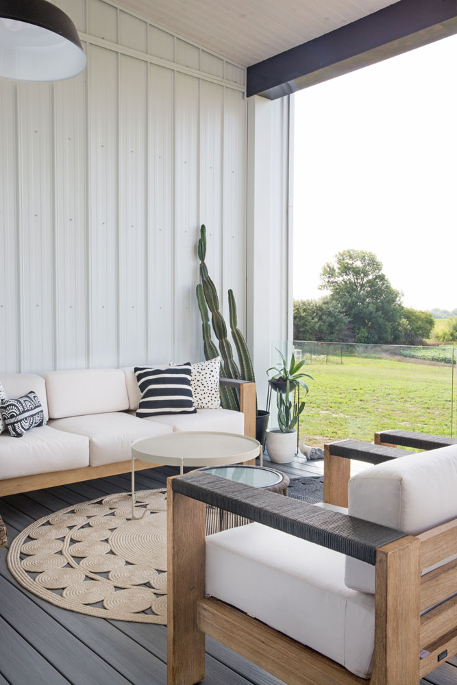 modern barn porch with white cushioned sofa and armchairs, cactus in corner