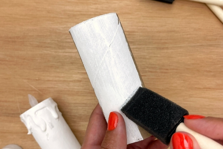 Person painting toilet paper rolls white for DIY craft