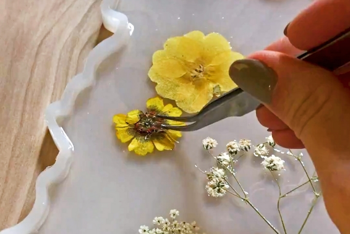 A close up of a person placing a dried yellow flower into a floral resin tray