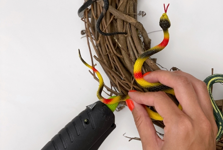 Person using a glue gun to stick a plastic snake on a wreath