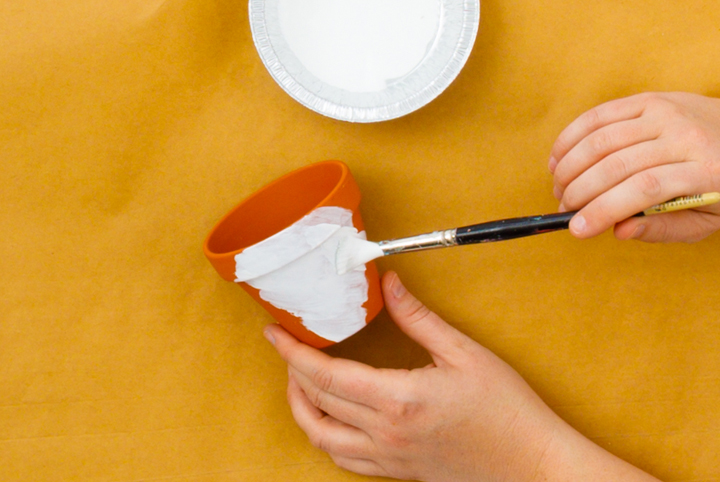 A person painting a terracotta pot white