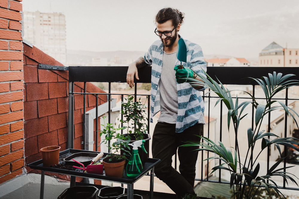 man looking at unplanted plants on apartment balcony