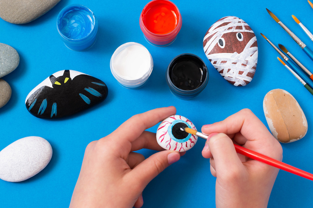 hands painting halloween designs on stones on blue background