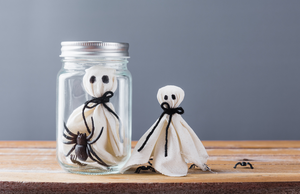 white ghost and spider in jar on wooden wall with grey background