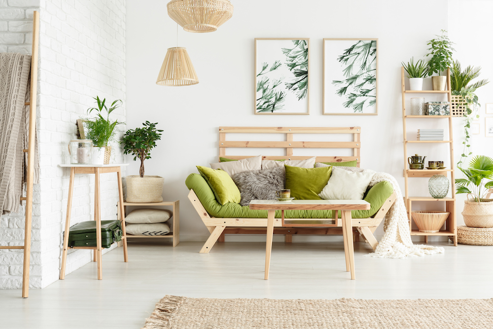 table and plants on wooden shelf in white living room with green sofa against wall with leaves posters