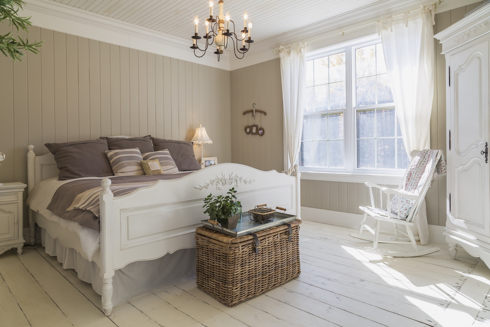 bedroom with double bed, cream-painted floorboards, brown wood panelled wall, white furniture and curtains