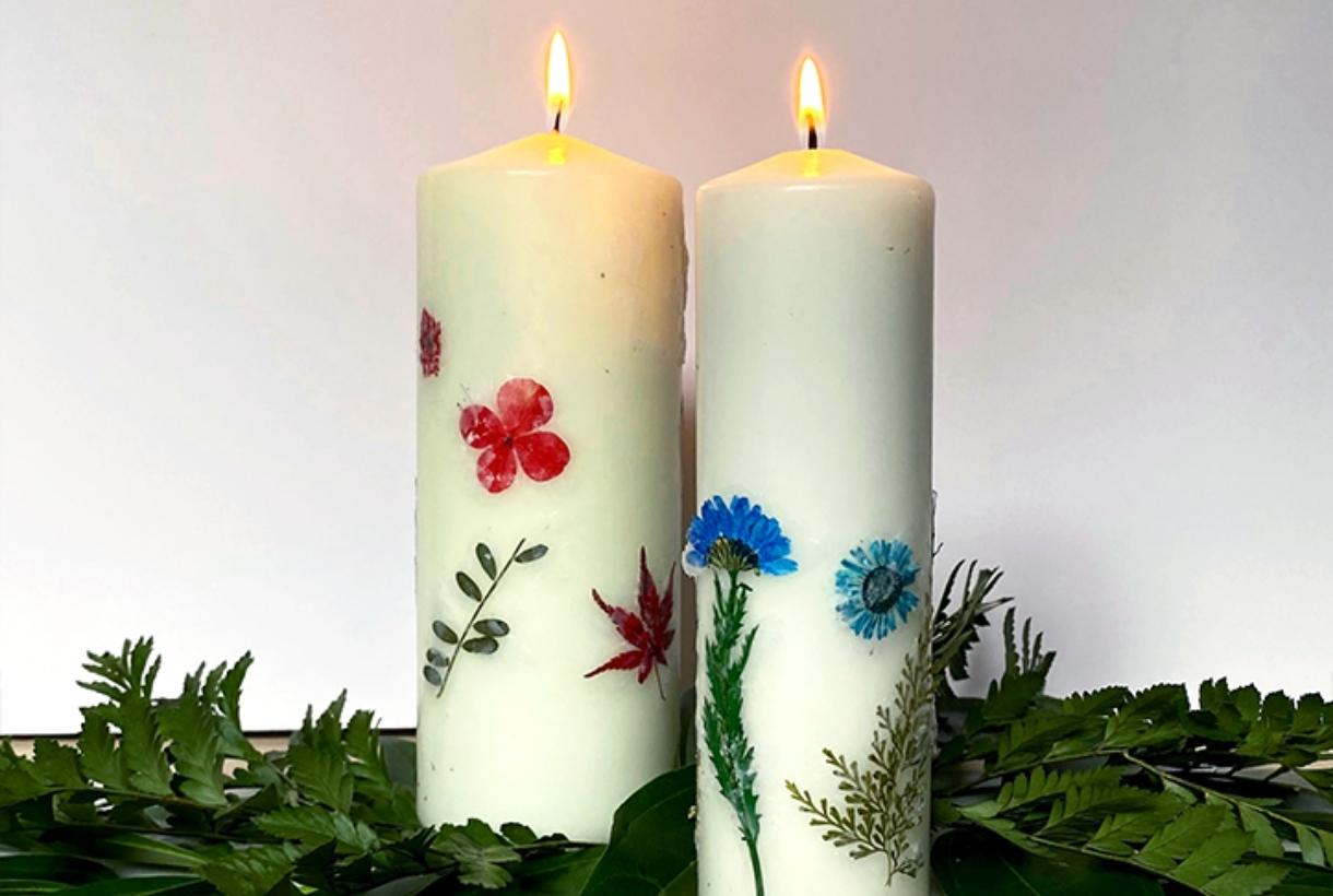 Two burningpressed floral candles surrounded by greenery