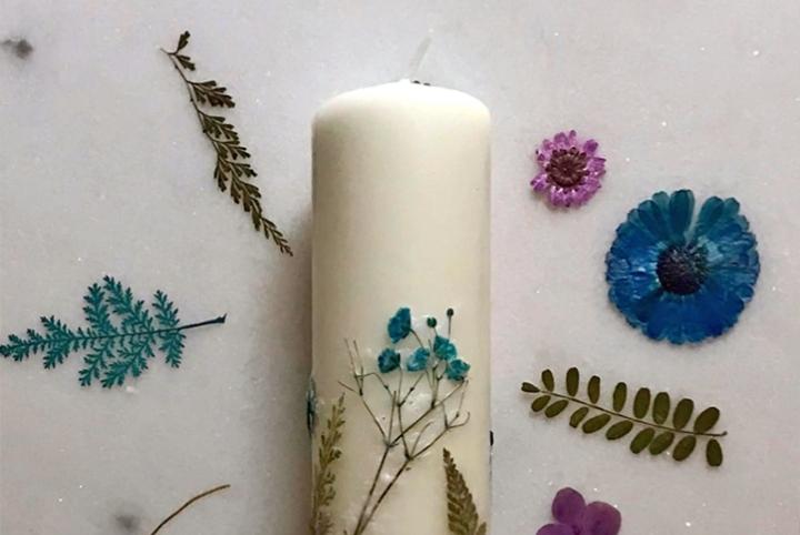 A white floral candle surrounded by dried flowers and greenery