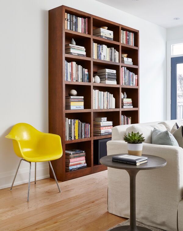 white wall with brown wooden freestanding book shelf unit and bright yellow chair