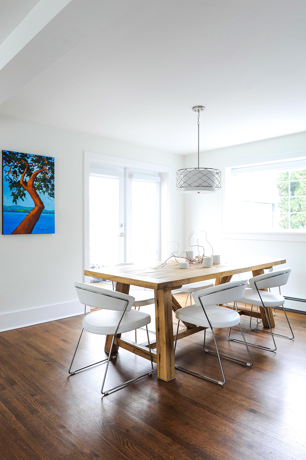 Modern eating area with oak trestle table and white leather chairs.
