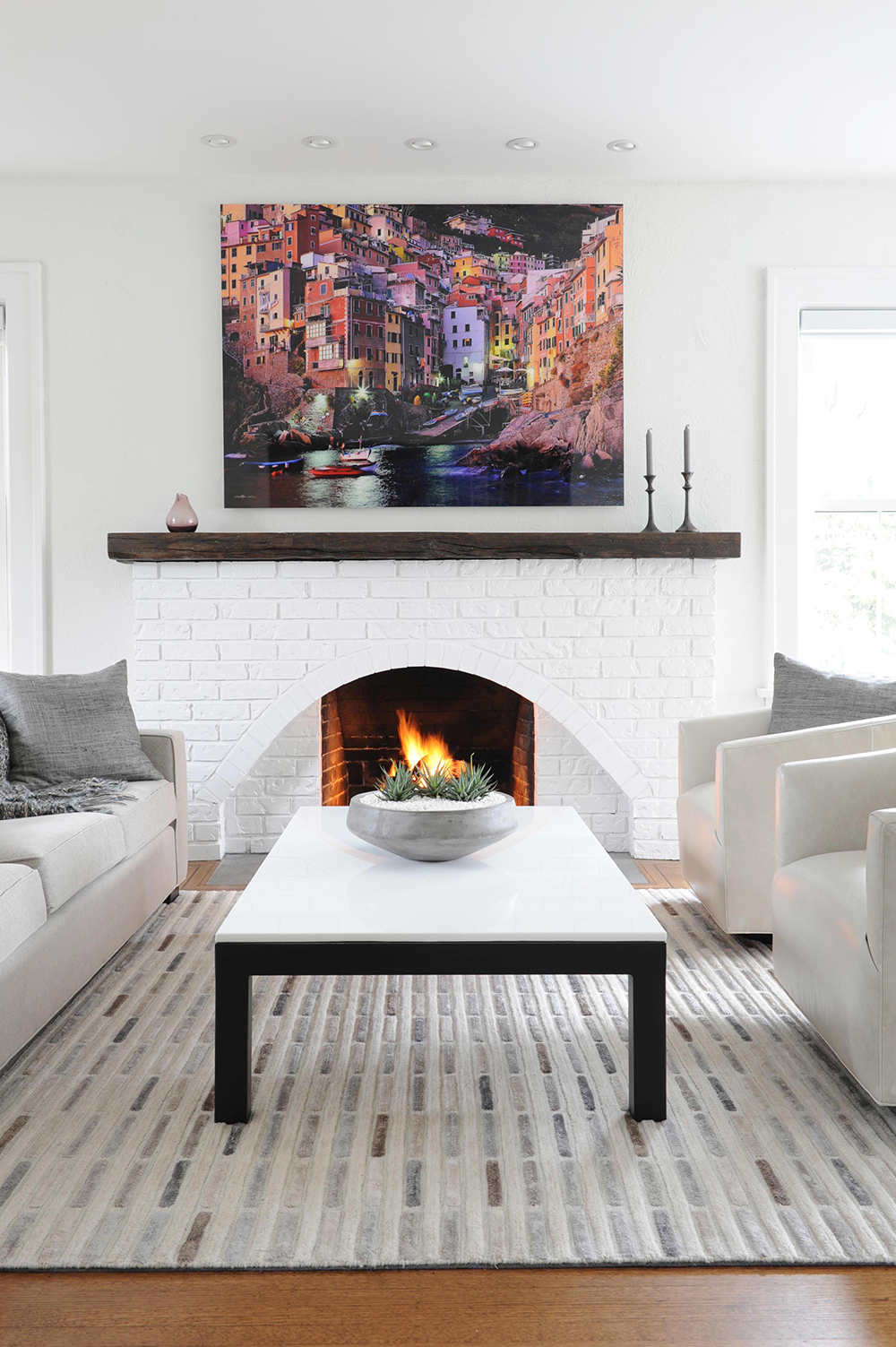 Large art piece of Italy's Cinque Terre hung above a brick fireplace.
