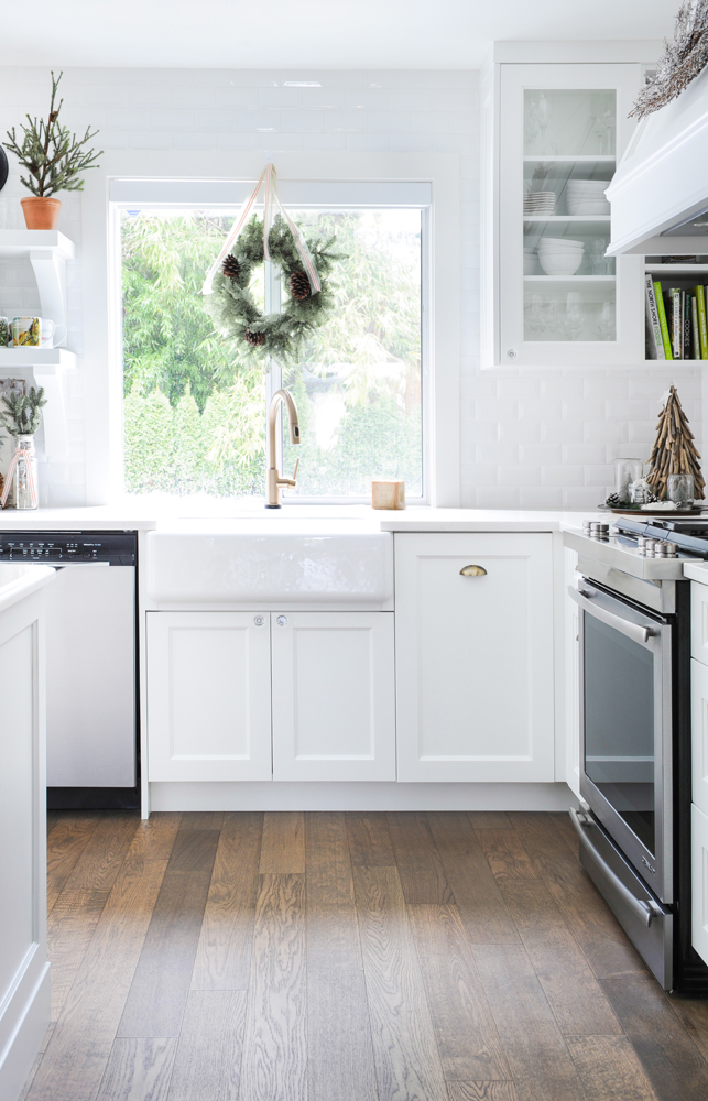 Modern white kitchen with farmhouse sink and holiday wreath hung above.