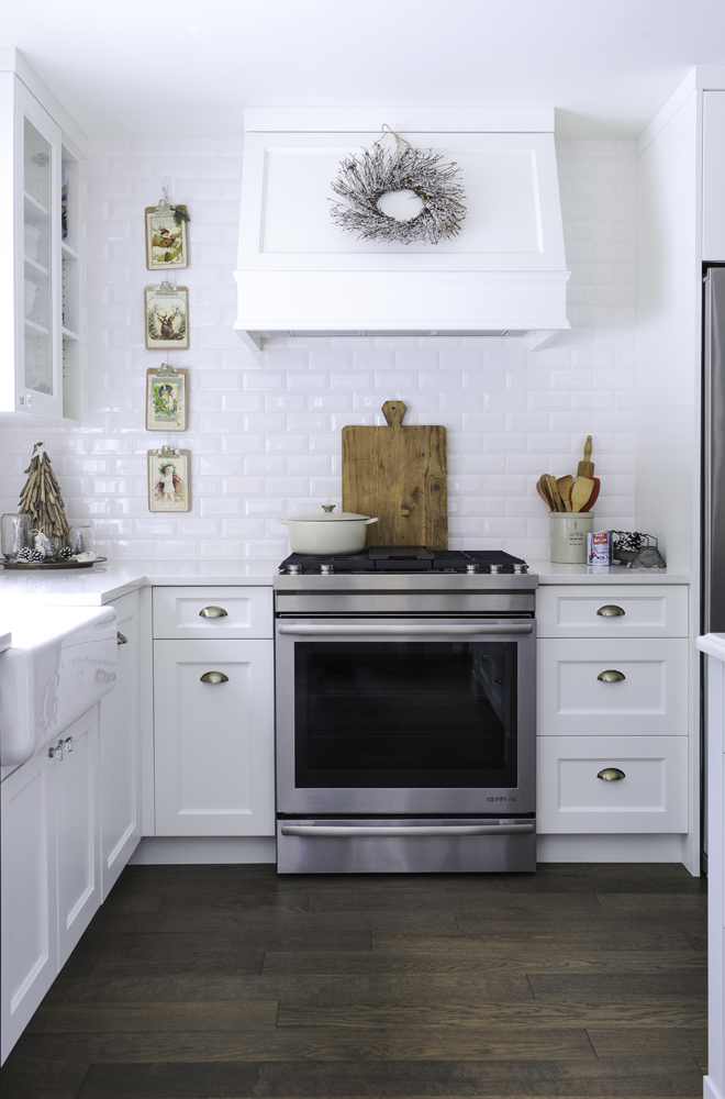 Modern white kitchen with holiday wreath hung on range hood.