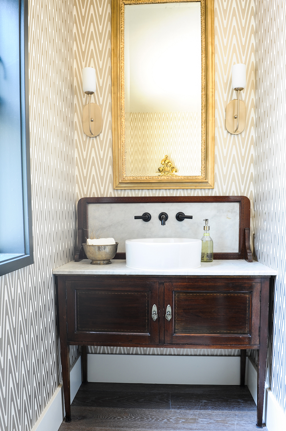 Powder room with wood vanity and gold striped wallpaper.