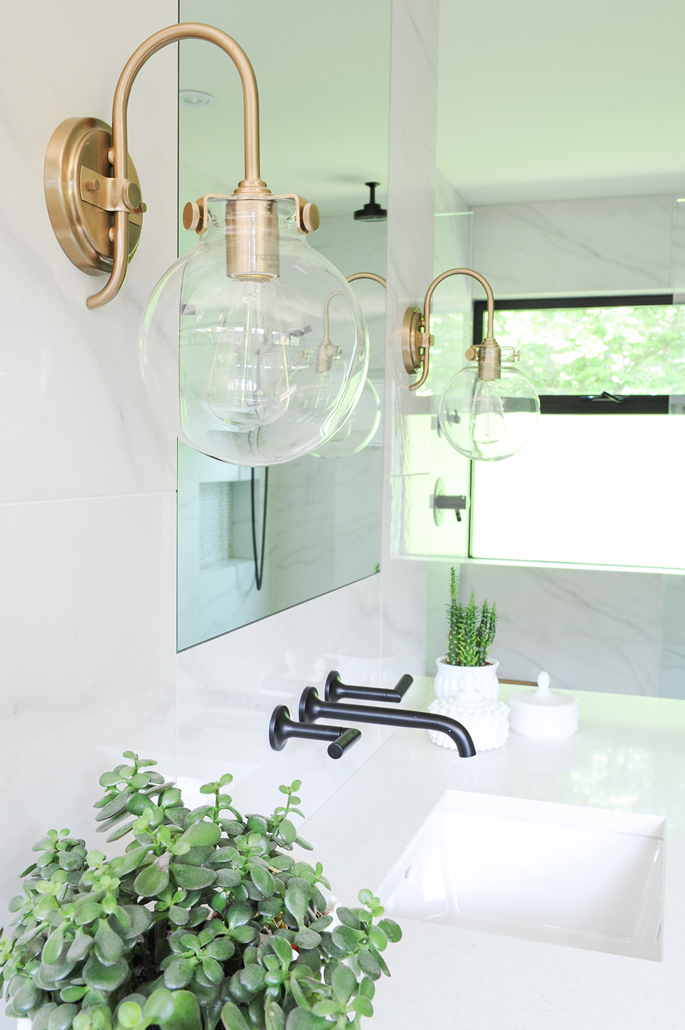 Brass sconces over sink with black faucet