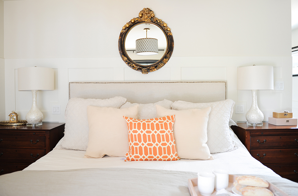 bedroom with orange cushion and round mirror over bed
