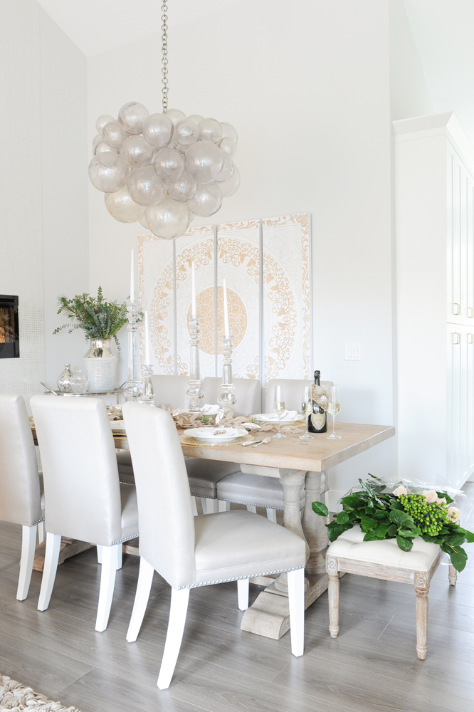 Dining area with chandelier in focus and cropped end of fireplace, white cabinets to the right