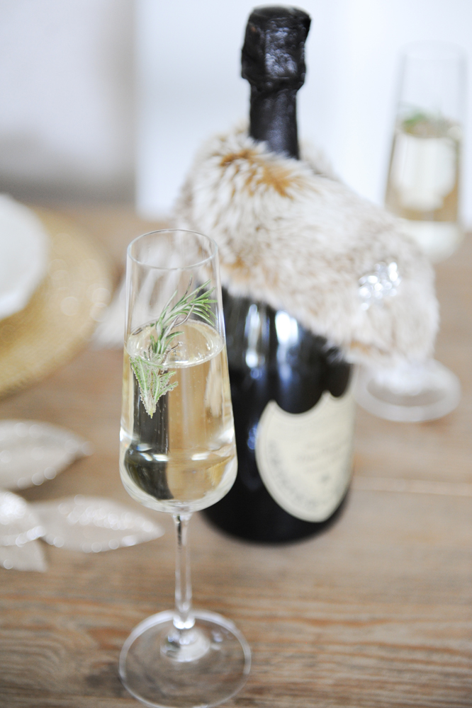 Champagne and rosemary in glass, champagne bottle behind
