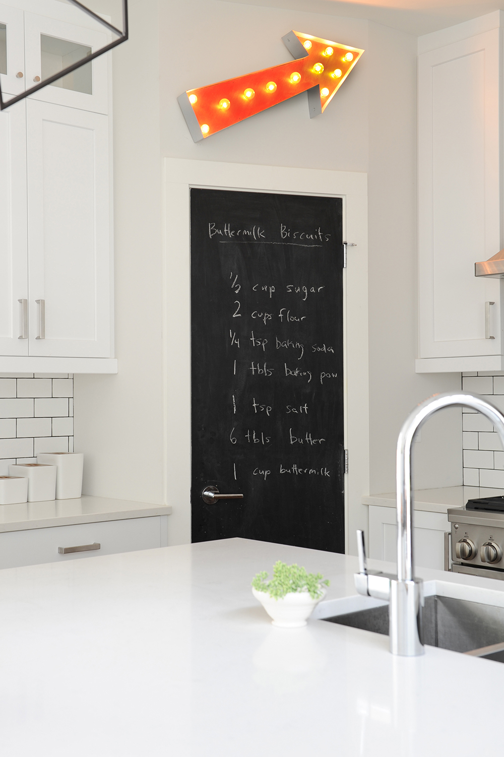 A modern white kitchen with a blackboard door.