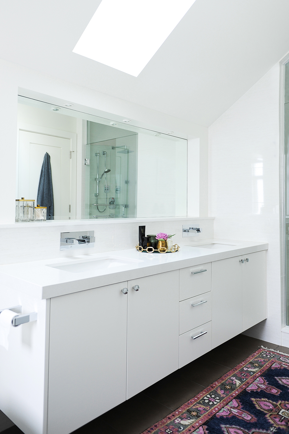A crisp white vanity is punctuated with a woven pattern rug and brass accents.