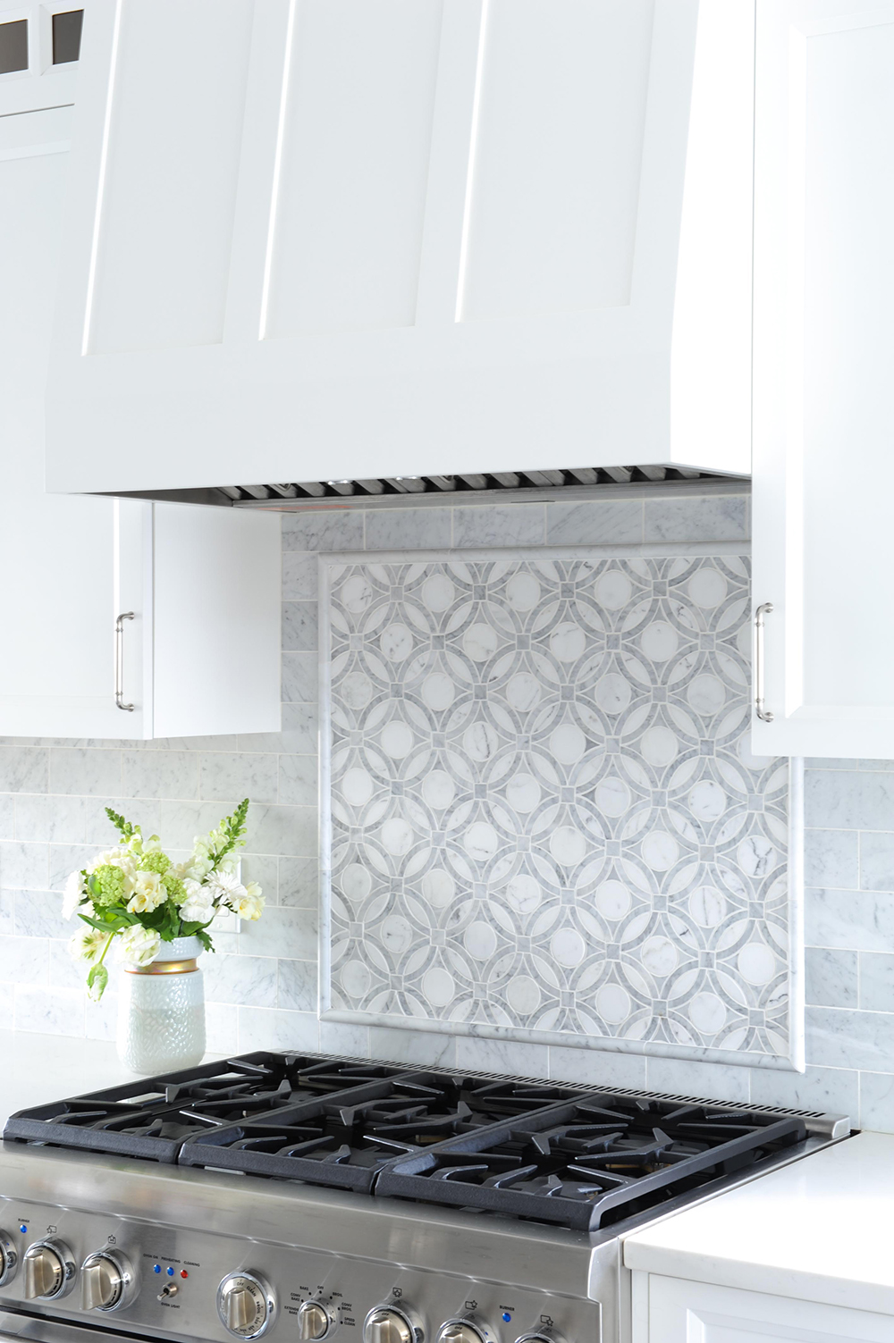 An intricate detail highlights the range in the all-white kitchen.