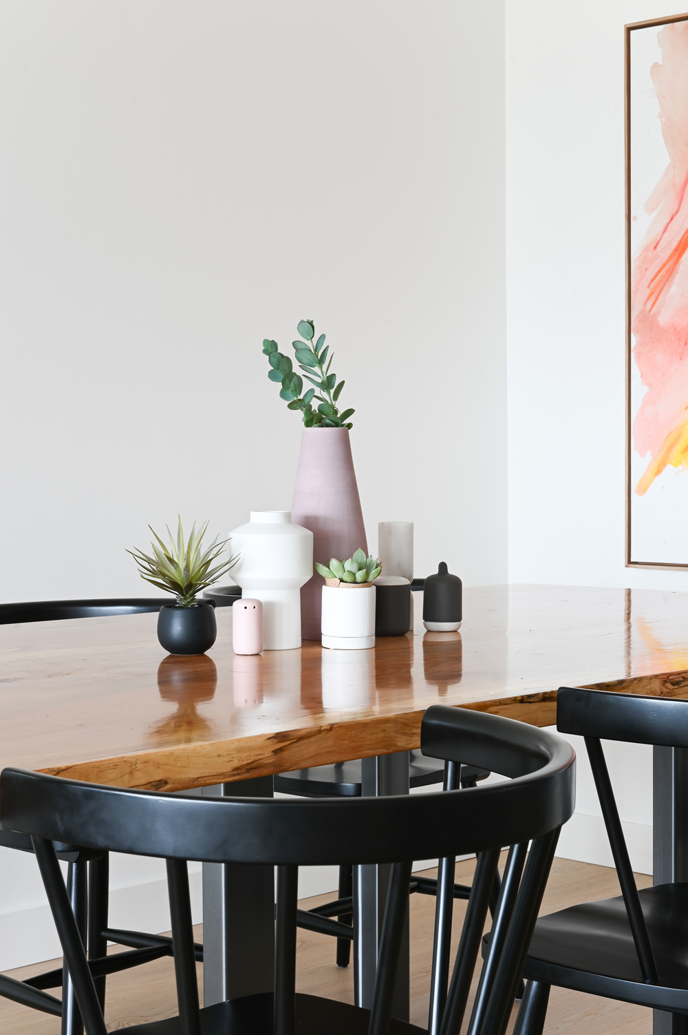 wood top dining table with pink white and black vessels and plants, black chairs