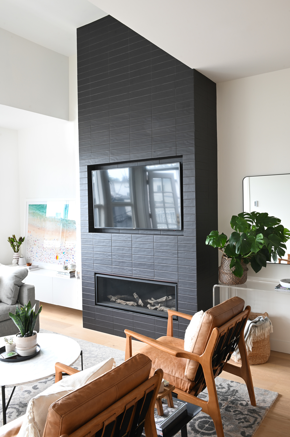 Black brick gas fireplace with TV inset and two tan and wood leather chairs in foreground