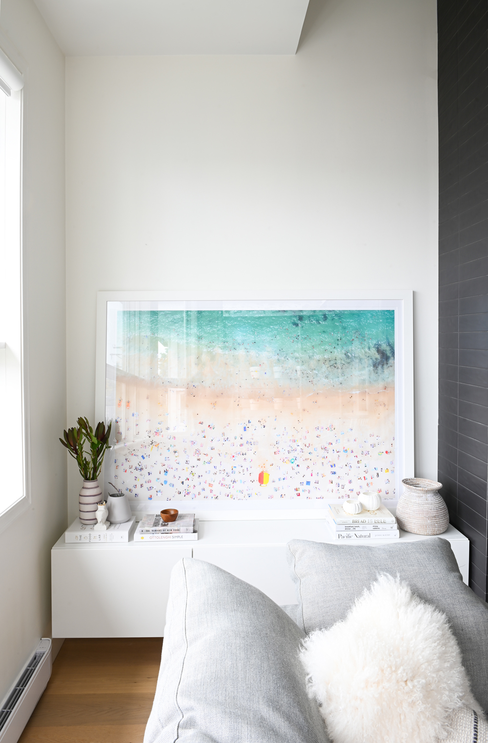 close up of beach artwork on white floating cabinets with grey sofa cushions and white furry cushions in foreground