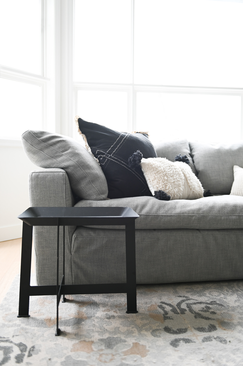 black side table in front of grey sofa with grey, black and white cushions