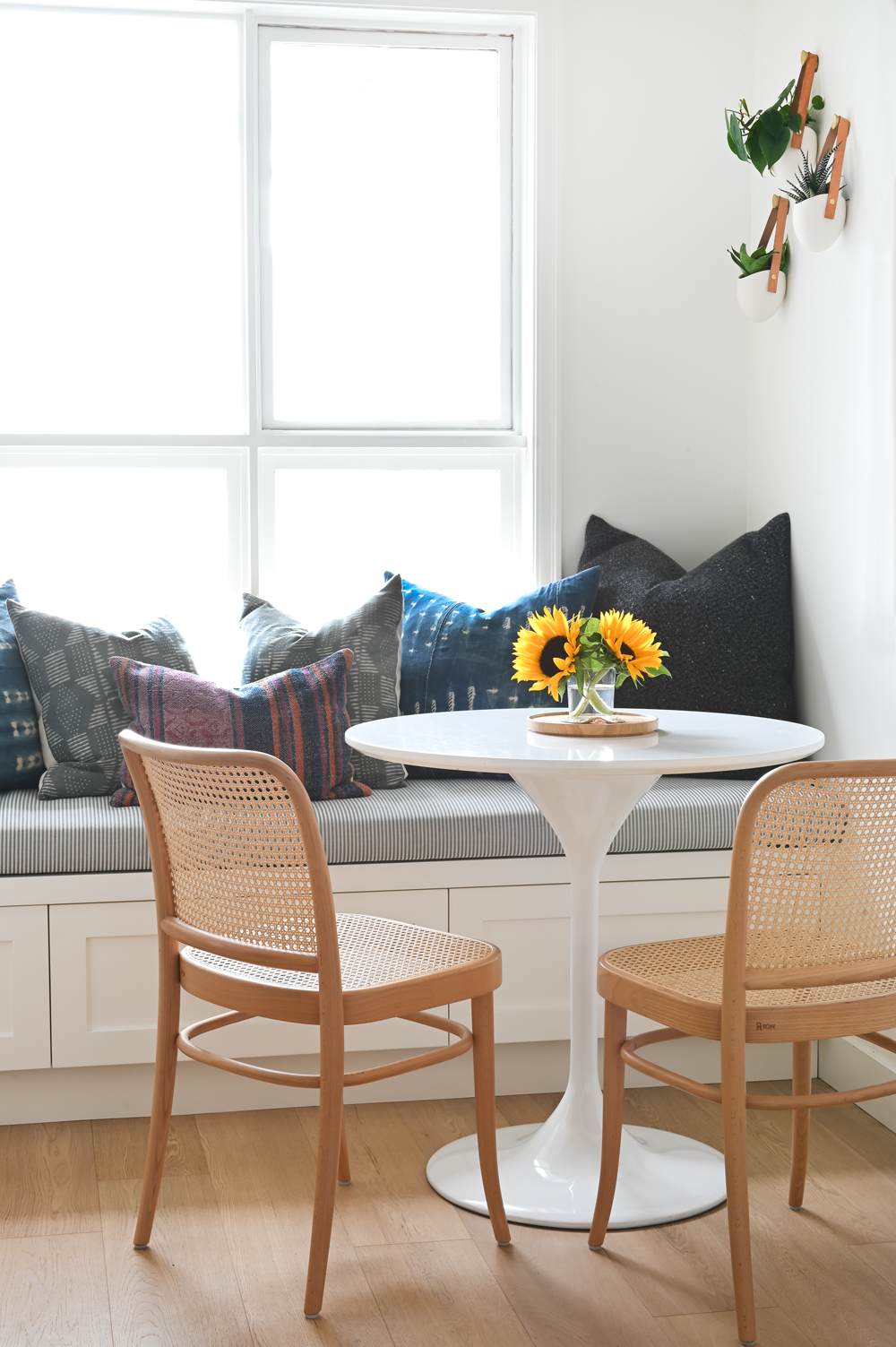 two cane chairs, white tulip table and built in bench with cushions in breakfast nook