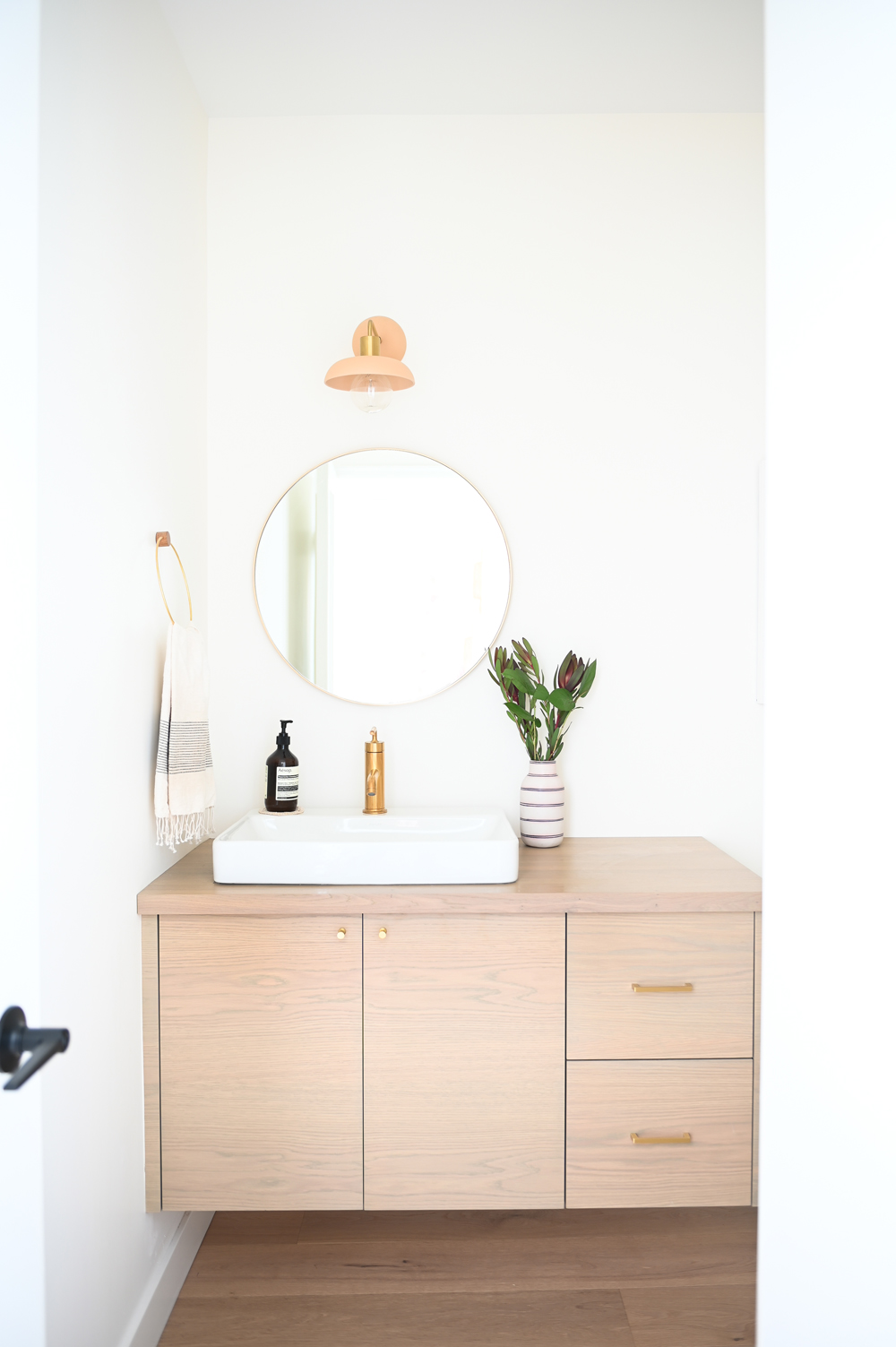 bathroom pale floating vanity with two cupboards and two drawers, white rectangular vessel sink, brass faucet, round mirror