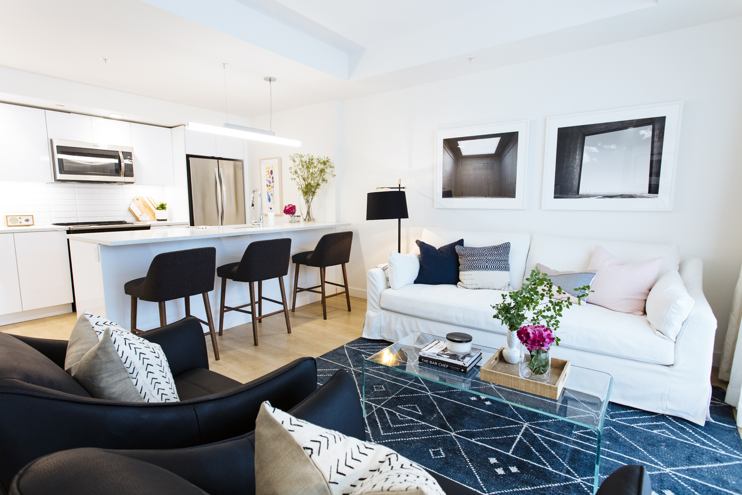 An open-concept living room and kitchen space with white and black furniture with a patterned blue rug