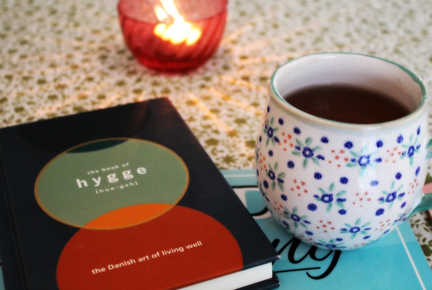 Book about Hygge on table with cup of tea and candle