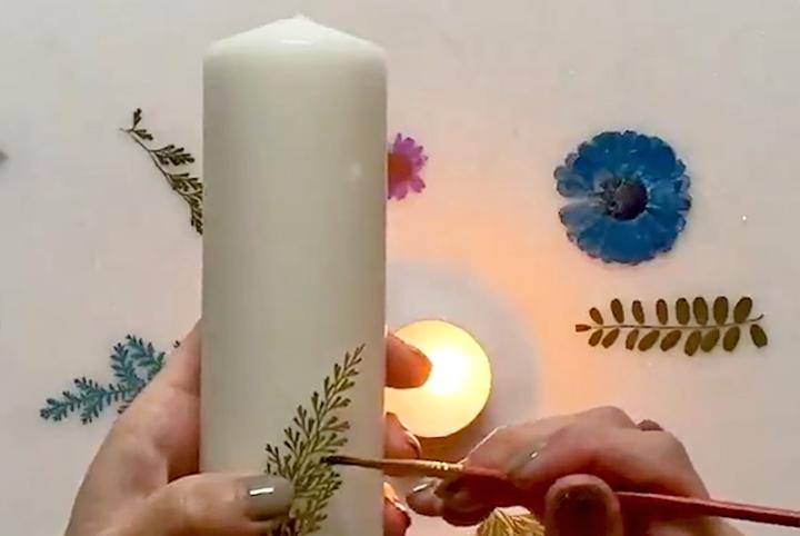 A person using a paint brush to stick a dried leaf onto a candle