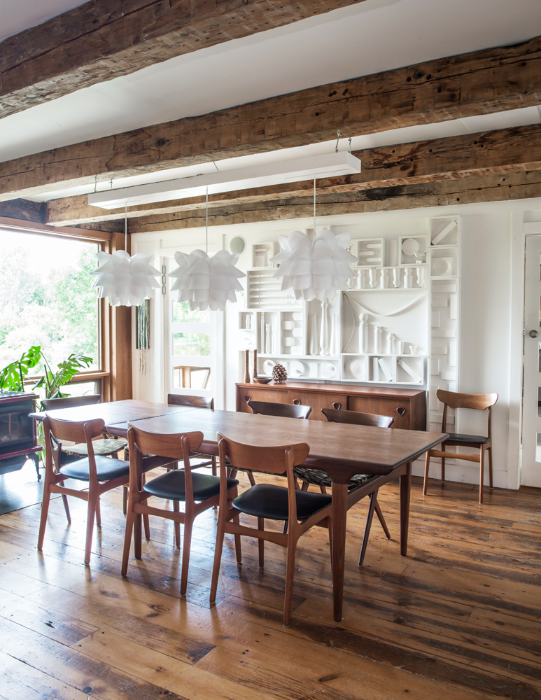 dining room with wood table, six wood chairs with black leather seats, three white artichoke chandeliers