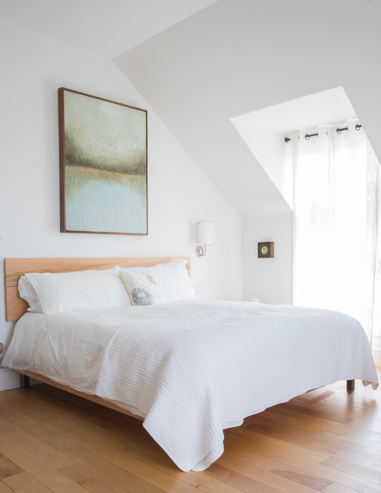 white bed in white bedroom with wood floor and abstract lake painting over bed