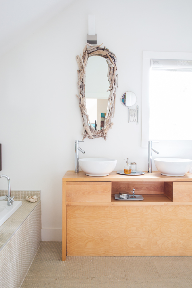white bathroom with tan mosaics and driftwood mirror over two vessel sinks